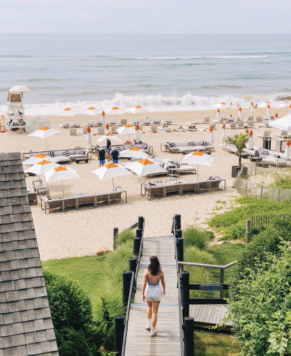 Boardwalk leading down to a Hamptons beach club lined with white and orange umbrellas