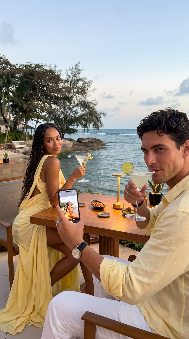 Couple toasting with cocktails at a seaside table at sunset